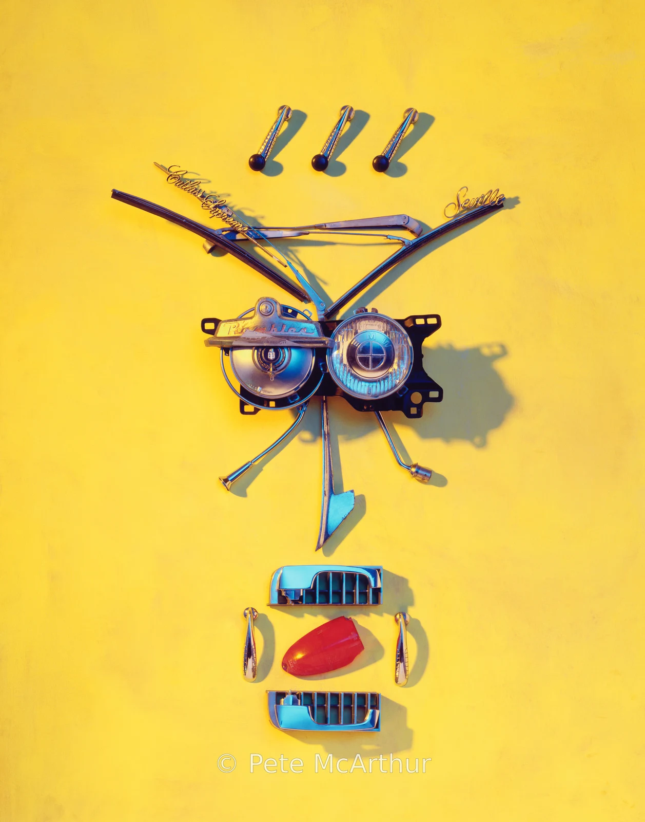 Assorted automotive parts are arranged to resemble a face against yellow.