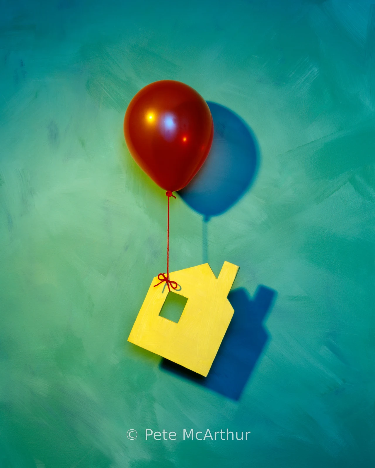 A red balloon is tied to a small yellow house-shaped cutout on teal.