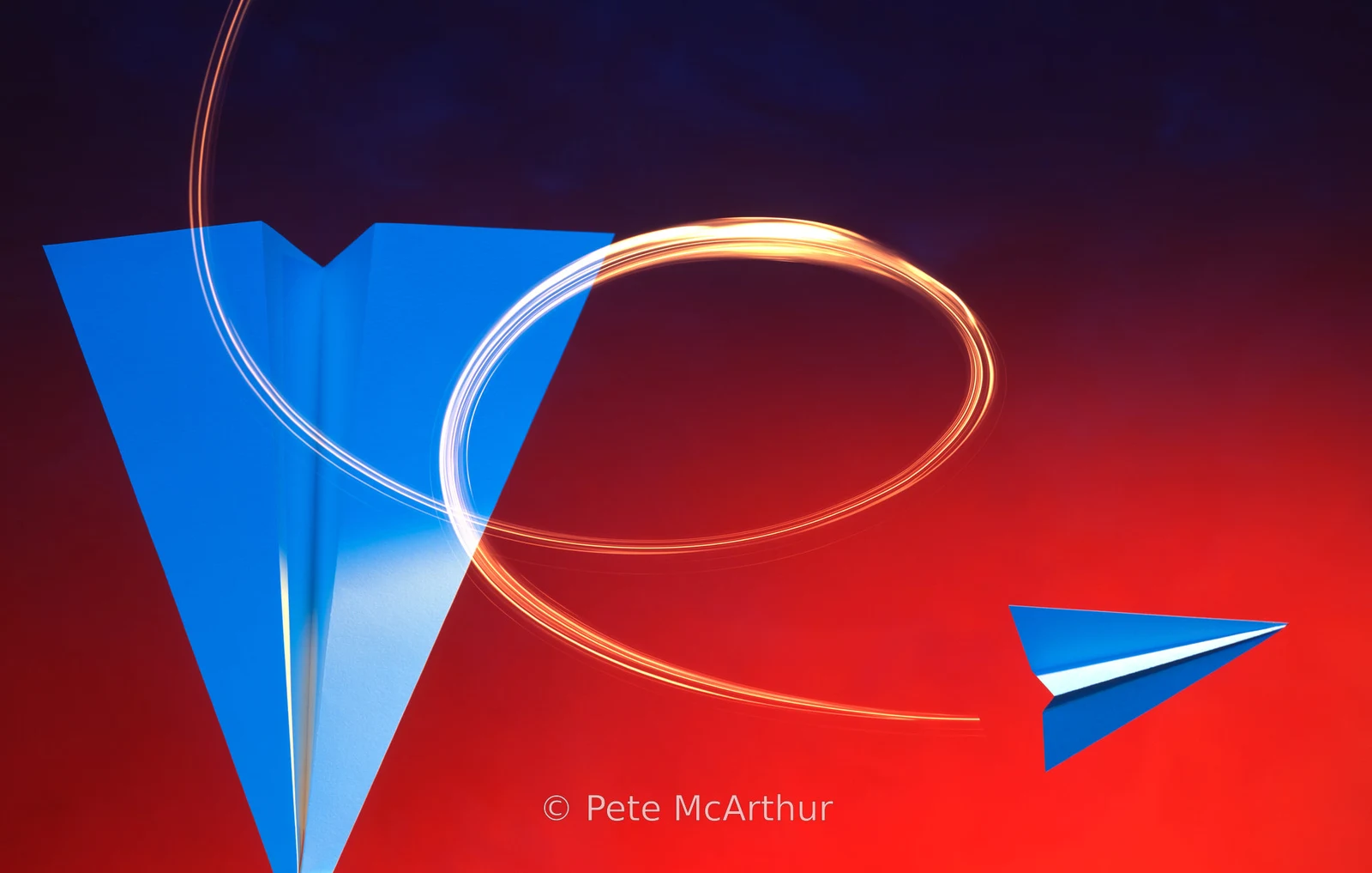 A small blue paper airplane passes a larger downward pointing plane with a curved light trail.
